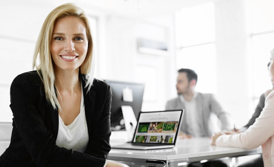 MoosMoos Verkäuferin sitzt am Konferenztisch mit aufgeklapptem Laptop und lächelt