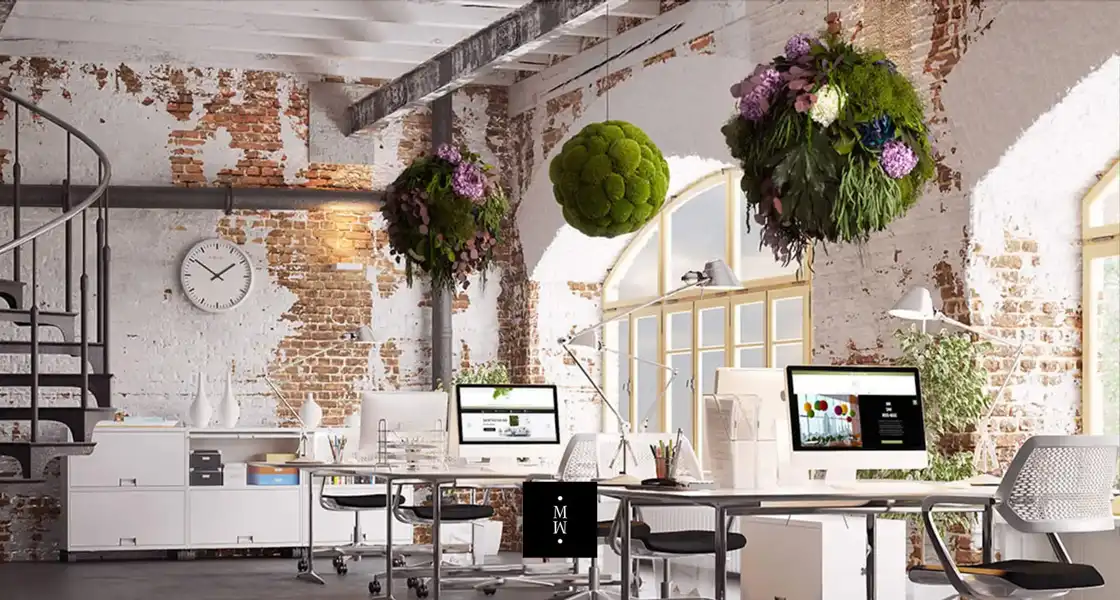 a room with a brick wall and a large desk with computers and plants from the ceiling