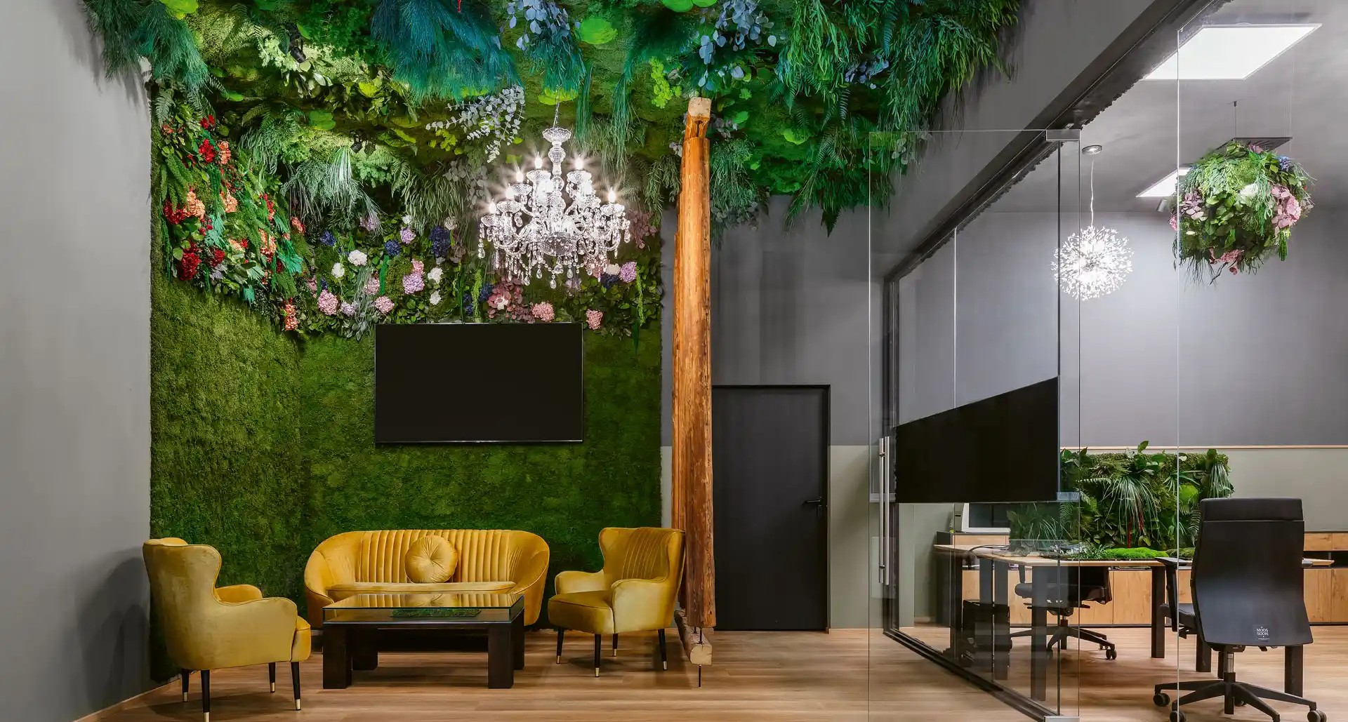 Bürolounge mit eleganter Dschungeldecke aus Moos und Pflanzenwand, kombiniert mit Kristallleuchter und modernen Sitzmöbeln, schafft eine natürliche und repräsentative Atmosphäre.
