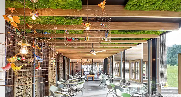 Helles Restaurant mit Holzdetails, Vogelkäfig-Lampen und einer lebendigen Decke aus Moos von MoosMoos für außergewöhnliches Raumdesign