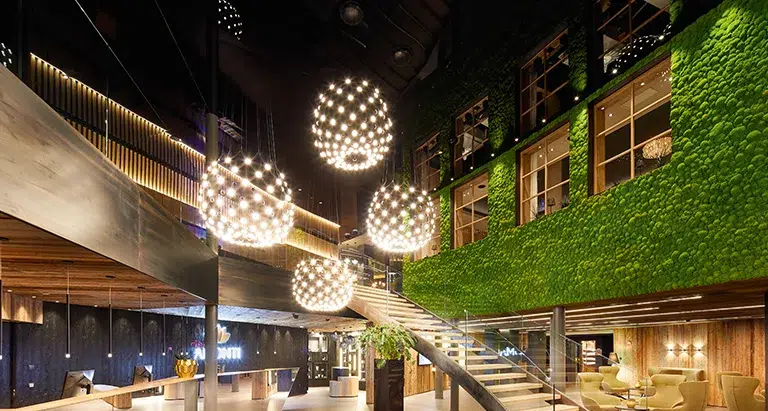 Große Hotellobby mit imposanter Wand aus Ballenmoos von MoosMoos, eleganter Treppe, modernen Leuchten und stilvollem Loungebereich