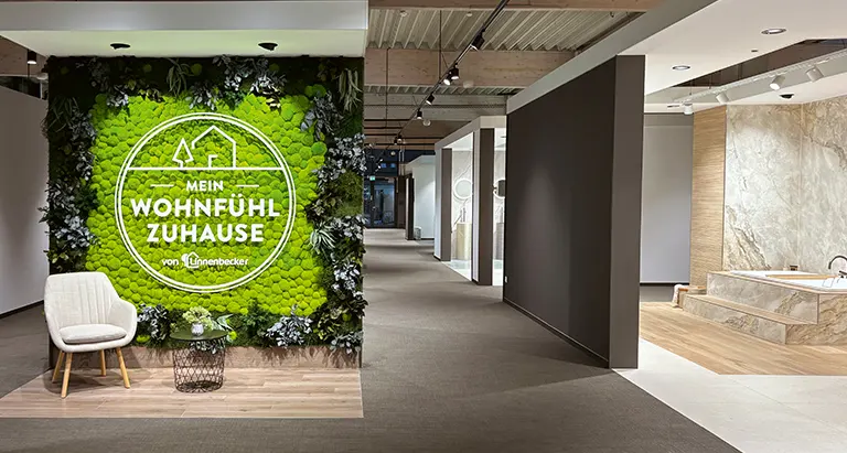 Grüne MoosMoos Wand aus Moos mit Logo „Mein Wohnfühl Zuhause“ – Naturdesign im Ausstellungsraum.