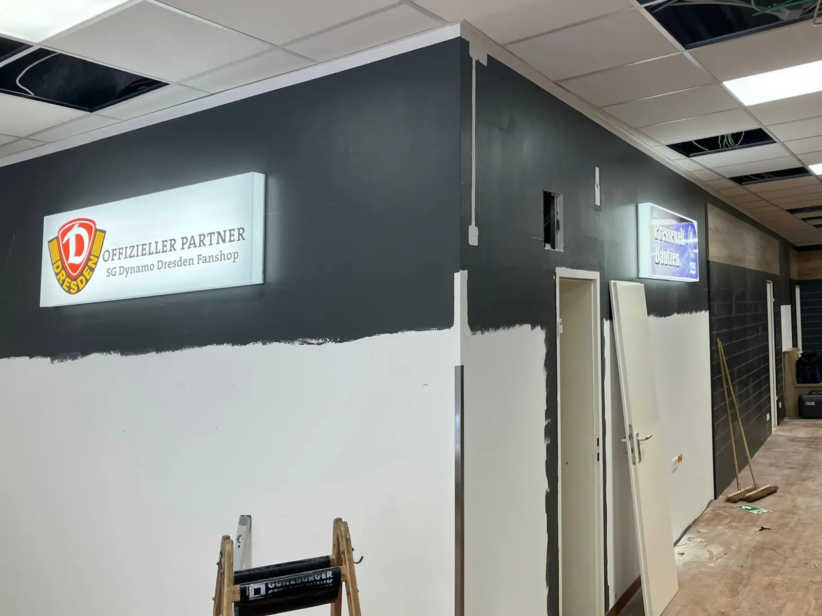 Presse Shop Bautzen während der Mooswand-Installation, graue Wand vor der Transformation mit MOOSMOOS Ballenmoos, Dynamo Dresden Fanshop Renovierung